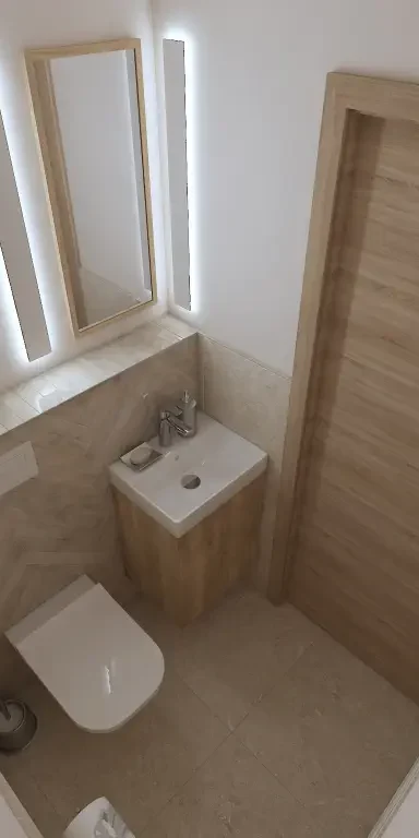 WC helyiség: halszálka mintás és nagy méretű kő mintás csempe burkolattal, kézmosóval, rejtett tartályos konzolos wc-vel - Társaházi lakás felújítása Budapest XII. kerületében